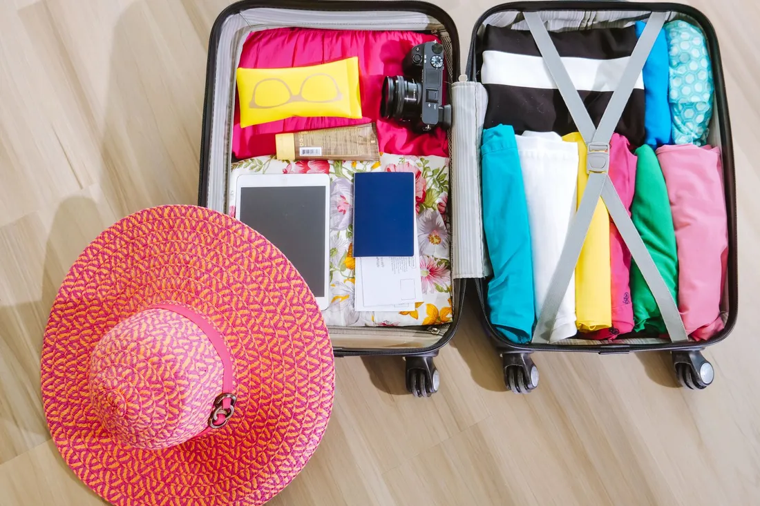 Gepackter Koffer mit Kleidung, Reisepass und Sonnenhut von oben fotografiert