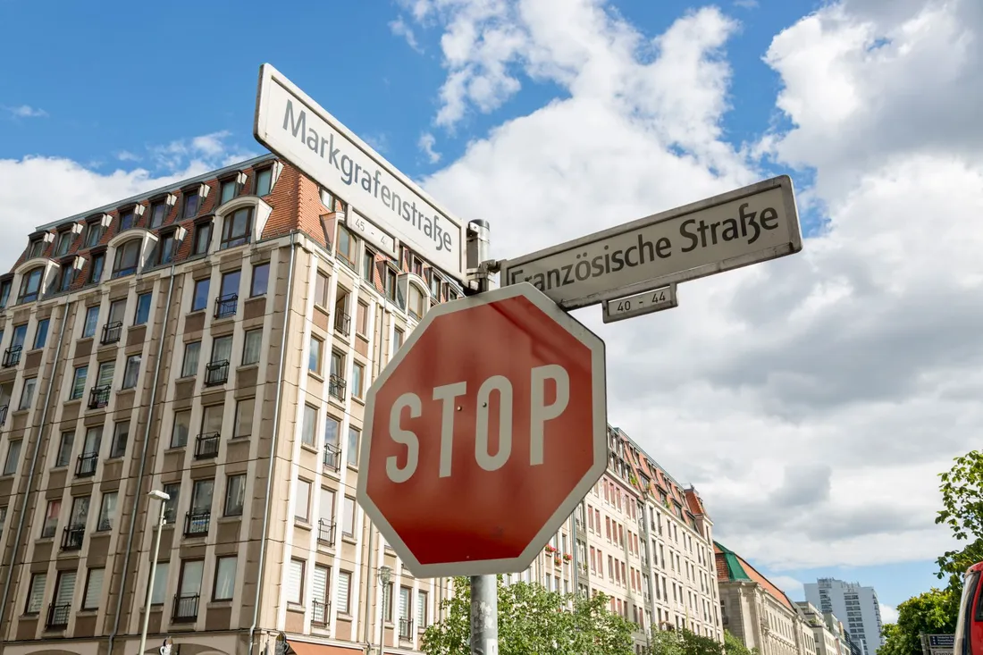 Stoppschild und zwei Straßenschilder vor hohen Altbaufassaden